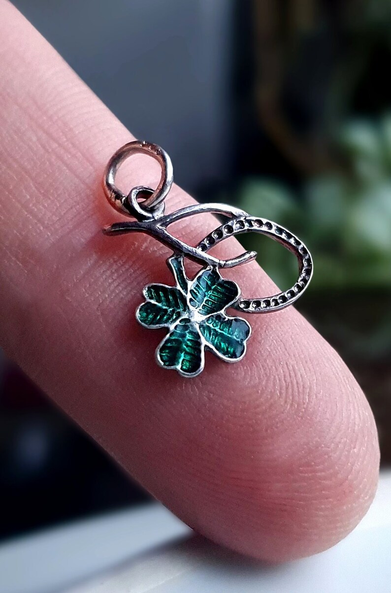 May include: A silver charm with a green four-leaf clover design. The clover is attached to a silver stem with a loop at the top for attaching to a bracelet or necklace.