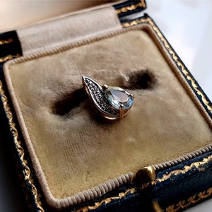 Peut inclure: Un pendentif délicat avec une pierre précieuse en aquamarine de forme poire entourée de diamants plus petits, sertie dans un motif de feuille d'or. Le pendentif est présenté dans un écrin à bijoux doublé de velours.