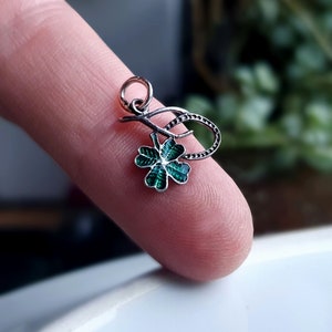 May include: A silver charm with a green four-leaf clover pendant. The clover is detailed with a textured surface and a silver stem.