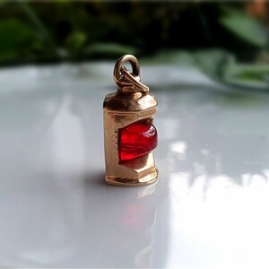 May include: A gold-toned charm in the shape of a red lantern. The lantern has a red glass window and a gold-toned metal frame.