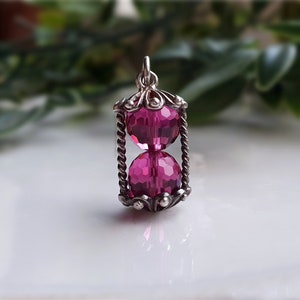 May include: A silver hourglass pendant with two pink faceted glass beads.