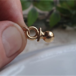 以下が含まれることがあります： ネックレスやブレスレットに取り付けられる、丸い輪っかが付いた金色のベビーラトルチャームです。