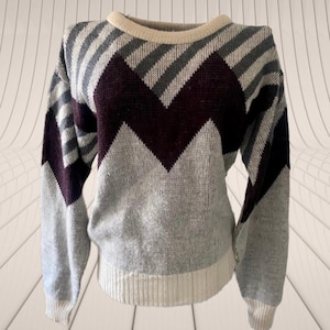May include: A gray, white, and burgundy chevron-patterned sweater. The sweater has a crew neck and ribbed cuffs and hem. The sleeves and upper chest feature a bold zigzag design, creating a striking visual contrast.