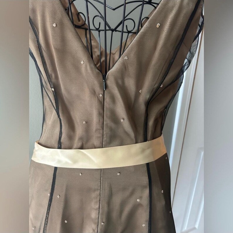 Puede incluir: Un vestido formal con escote en V y corpi&ntilde;o color champ&aacute;n. El vestido presenta una capa transparente negra con adornos dispersos y un cintur&oacute;n ancho de sat&eacute;n color crema. El vestido est&aacute; dise&ntilde;ado para ocasiones especiales.