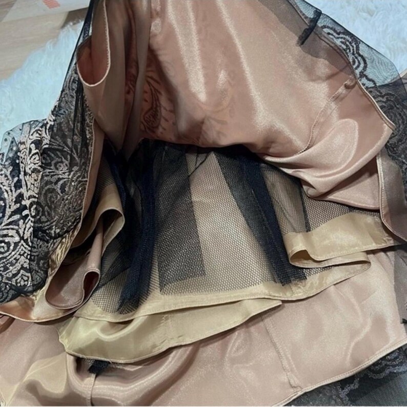 Puede incluir: Primer plano de un vestido formal con capas de tela. El vestido presenta una capa inferior de color champ&aacute;n satinado, una capa de tul negro y una superposici&oacute;n de encaje negro con un estampado floral. El vestido parece nuevo.