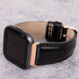 May include: A black leather watch band with a rose gold buckle and a gray smartwatch face.