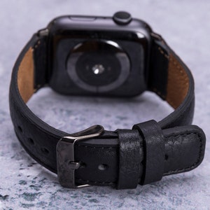 May include: Black leather watch band with a black metal buckle. The band is designed for an Apple Watch.