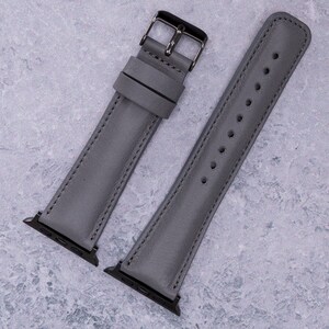 May include: Two gray leather watch bands with silver hardware. The bands are laid out flat on a gray textured surface.
