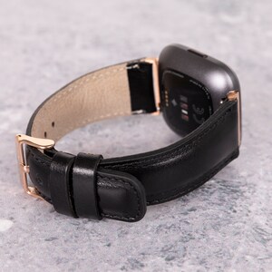 May include: A black leather watch band with a rose gold buckle and a gray smartwatch face.