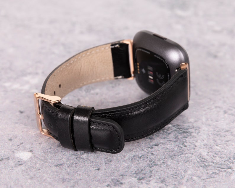 May include: A black leather watch band with a rose gold buckle and a gray smartwatch face.