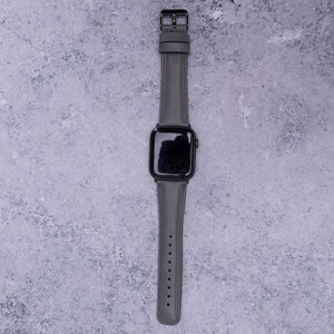 May include: A gray leather watch band with a black Apple Watch face.