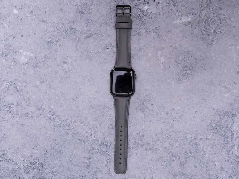 May include: A gray leather watch band with a black Apple Watch face.