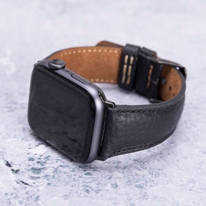 May include: A black leather watch band with a silver buckle and a black Apple Watch face.