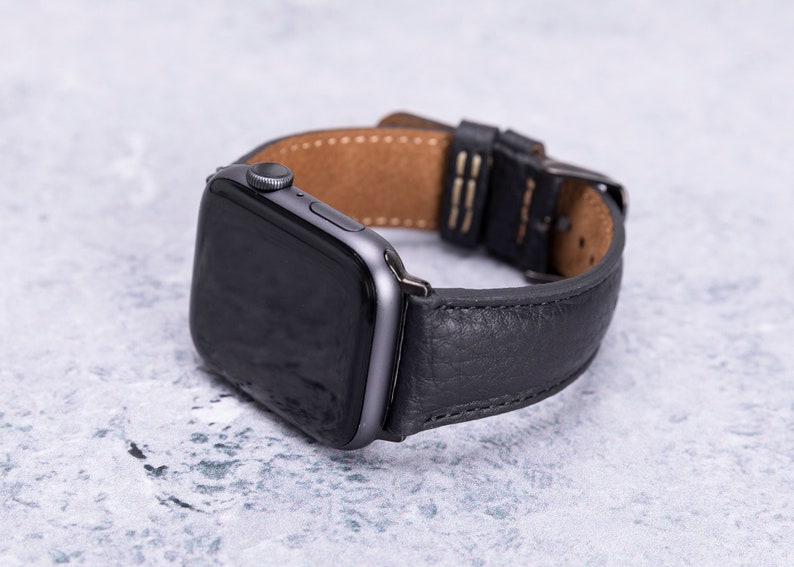 May include: A black leather watch band with a silver buckle and a black Apple Watch face.