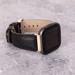 May include: A black leather watch band with a rose gold accent and a black smartwatch face.