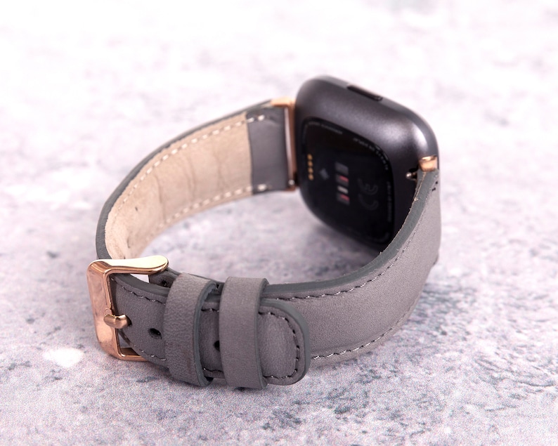 May include: A gray leather watch band with rose gold hardware. The band is designed for a smartwatch with a square face.