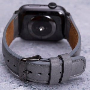 May include: A gray leather watch band with a black metal buckle. The band is designed for a smartwatch with a round face.