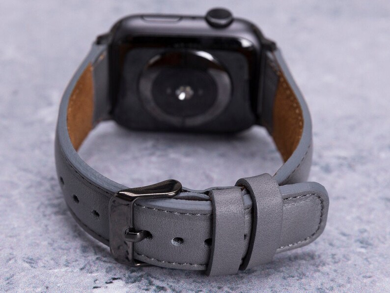 May include: A gray leather watch band with a black metal buckle. The band is designed for a smartwatch with a round face.