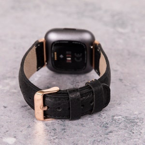 May include: A black leather watch band with a rose gold buckle and a silver smartwatch face.