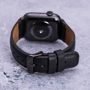 May include: Black leather watch band with a black metal buckle and a black smartwatch face.