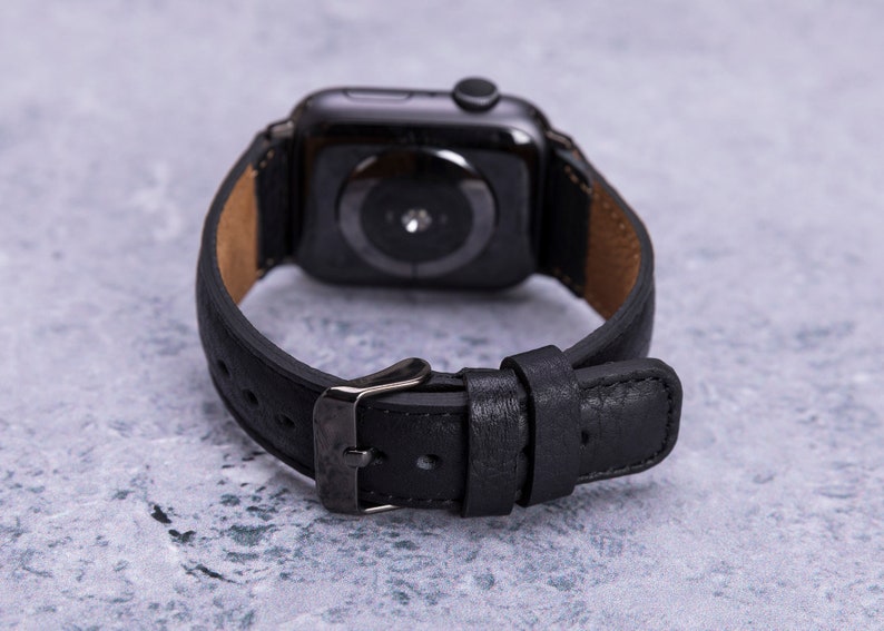May include: Black leather watch band with a black metal buckle and a black smartwatch face.