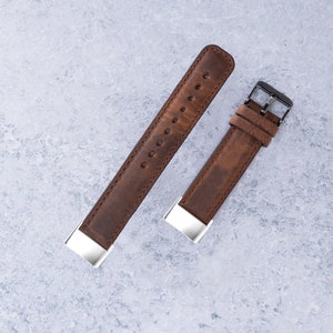 May include: Two brown leather watch straps with silver buckles. The strap on the left is longer than the strap on the right.
