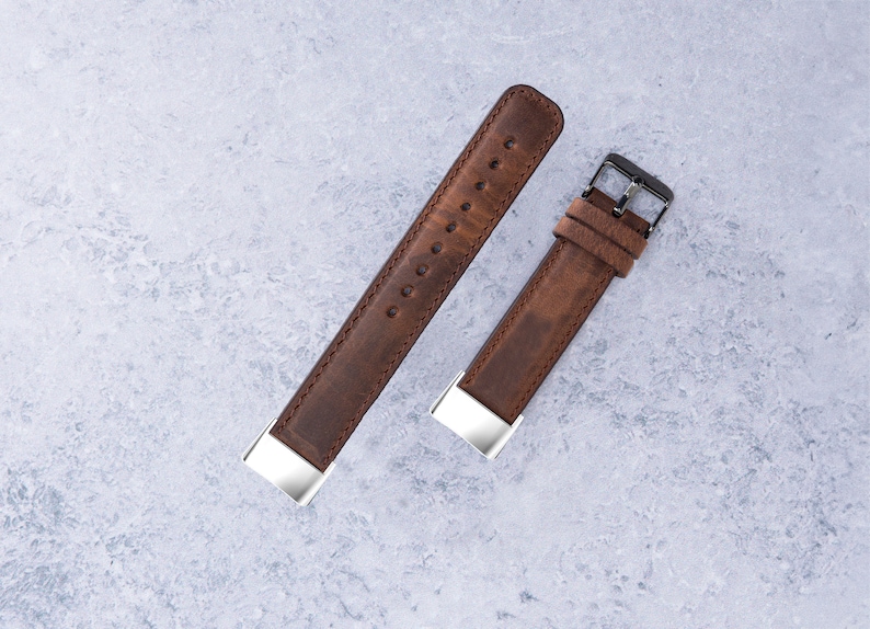 May include: Two brown leather watch straps with silver buckles. The strap on the left is longer than the strap on the right.