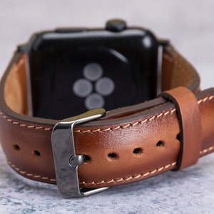 May include: A brown leather watch band with a silver buckle and stitching. The band is attached to a black smartwatch with a black screen.