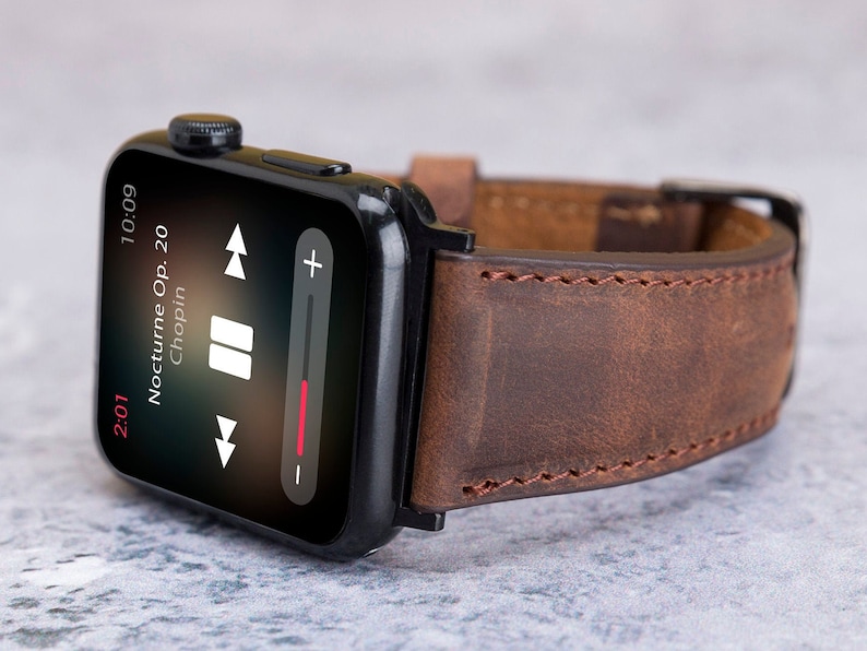 May include: A black Apple Watch with a brown leather strap. The watch face shows a music player with the song "Nocturne Op. 20 Chopin" playing.