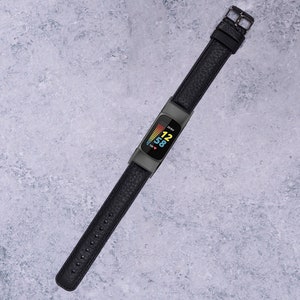 May include: A black fitness tracker with a black leather band. The screen displays the time, 12:58, and a heart rate graph.