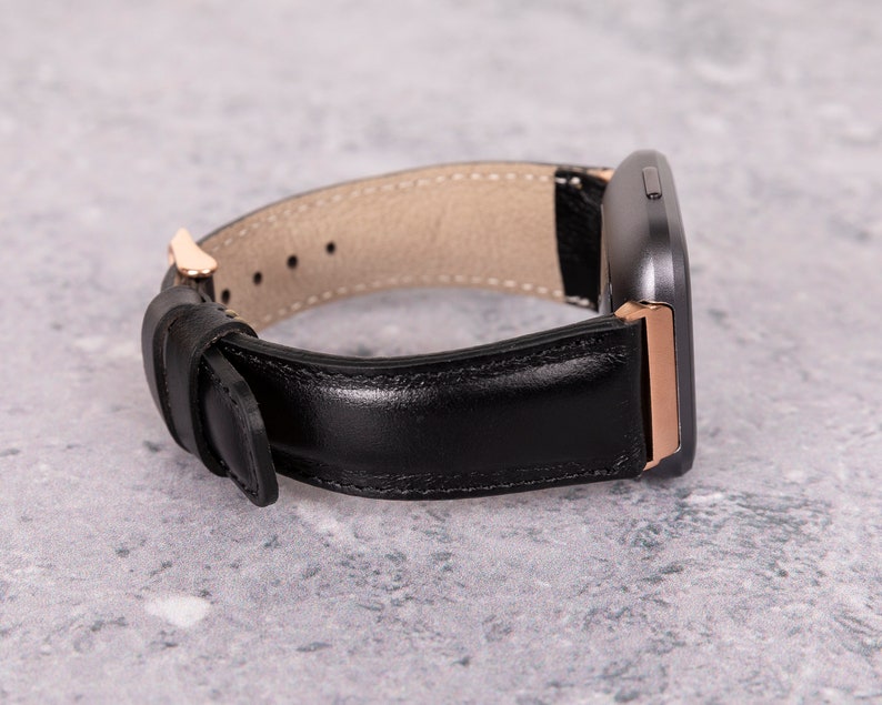 May include: A black leather watch band with a rose gold buckle and a dark gray watch face.