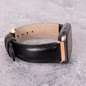 May include: A black leather watch band with a rose gold buckle and a gray smartwatch.