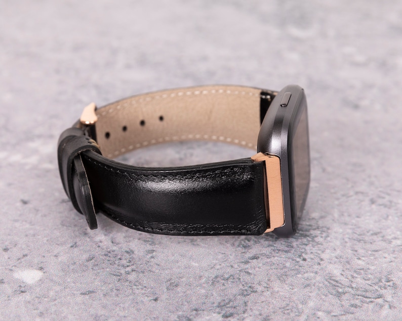 May include: A black leather watch band with a rose gold buckle and a gray smartwatch.