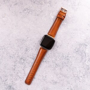Puede incluir: Una correa de reloj de cuero marr&oacute;n con una esfera cuadrada negra.