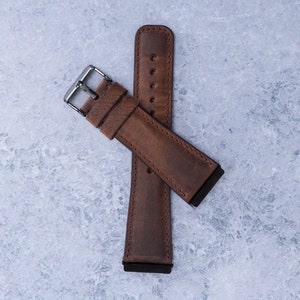 May include: A brown leather watch strap with a silver buckle. The strap is folded in half and the buckle is closed.