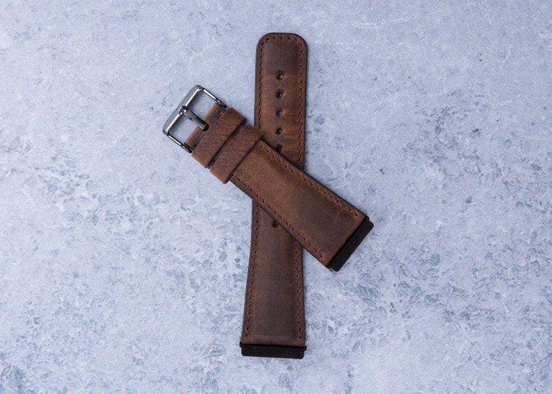 May include: A brown leather watch strap with a silver buckle. The strap is folded in half and the buckle is closed.