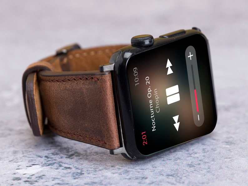 May include: A black smartwatch with a brown leather strap playing music. The screen shows "Nocturne Op. 20 Chopin" and the time 10:09. The music player controls are visible on the screen.