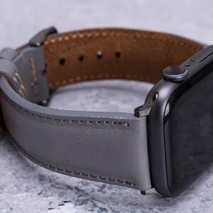 May include: A gray leather watch band with brown leather lining, designed for an Apple Watch.