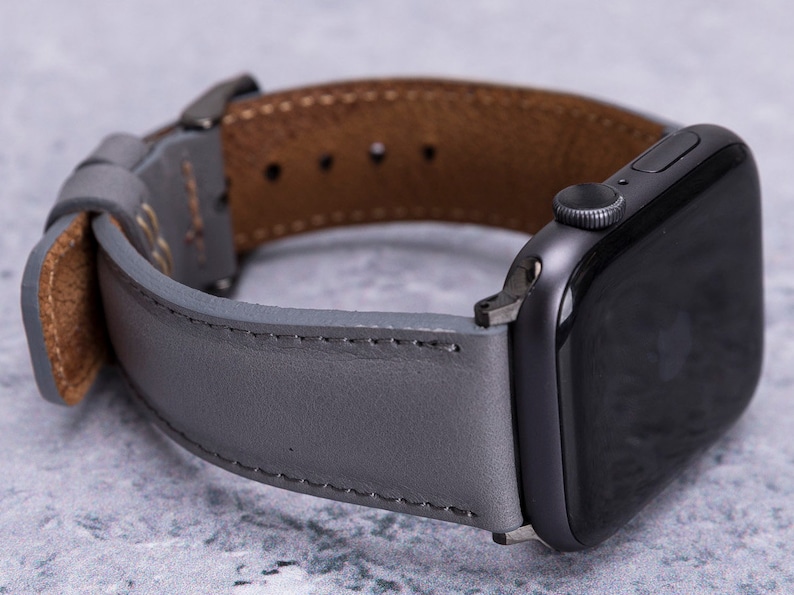 May include: A gray leather watch band with brown leather lining, designed for an Apple Watch.