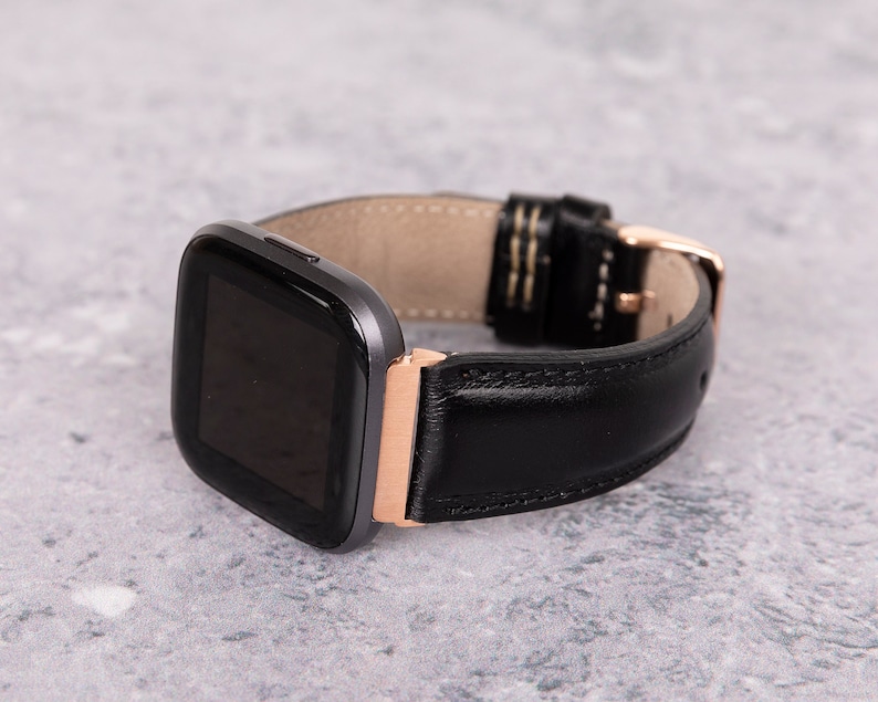 May include: A black leather watch band with a rose gold buckle and a gray smartwatch face.