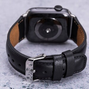 May include: Black leather watch band with a silver buckle. The band is designed for a smartwatch with a round face.