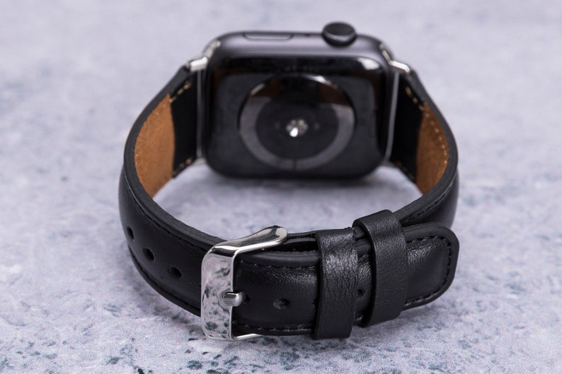 May include: Black leather watch band with a silver buckle. The band is designed for a smartwatch with a round face.