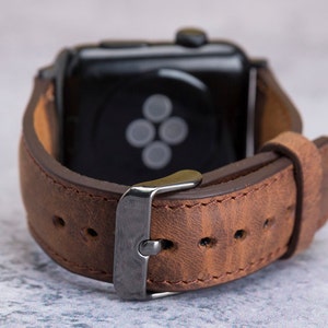 May include: A brown leather watch band with a silver buckle. The band is designed for a smartwatch with a black face.