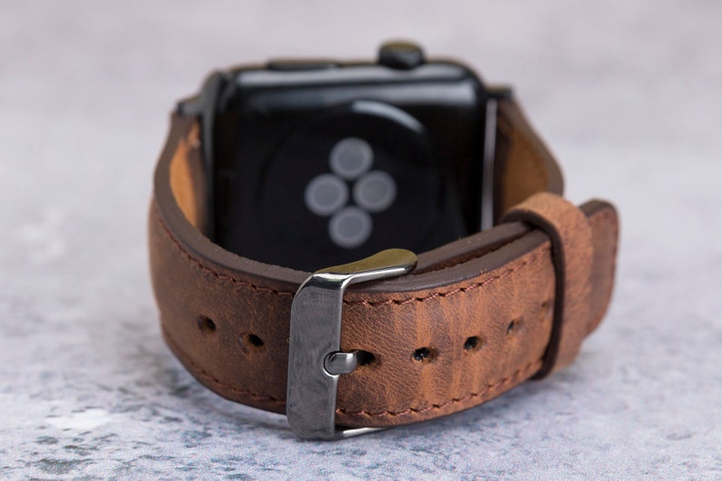 May include: A brown leather watch band with a silver buckle. The band is designed for a smartwatch with a black face.