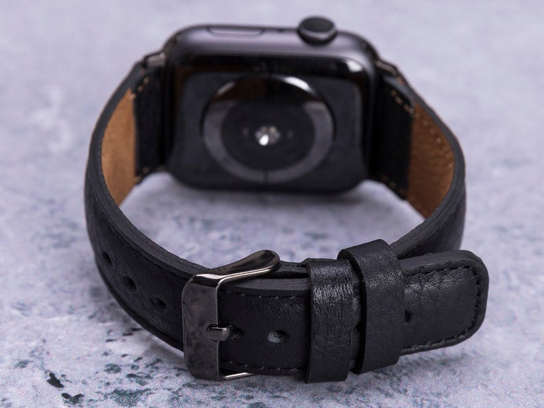 以下が含まれることがあります： 銀色のバックルが付いた黒い革製の腕時計バンド。バンドはApple Watch用に設計されています。