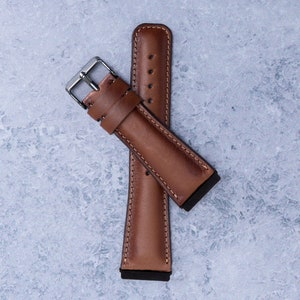 May include: A brown leather watch strap with a silver buckle. The strap is folded in half and the buckle is visible.