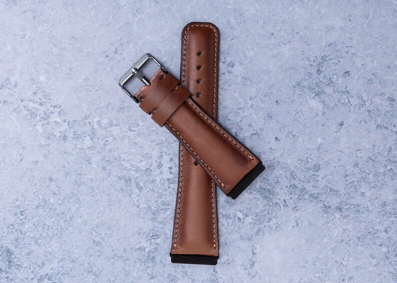 May include: A brown leather watch strap with a silver buckle. The strap is folded in half and the buckle is visible.