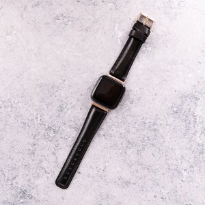 May include: A black leather watch band with a gold buckle and a black square watch face.