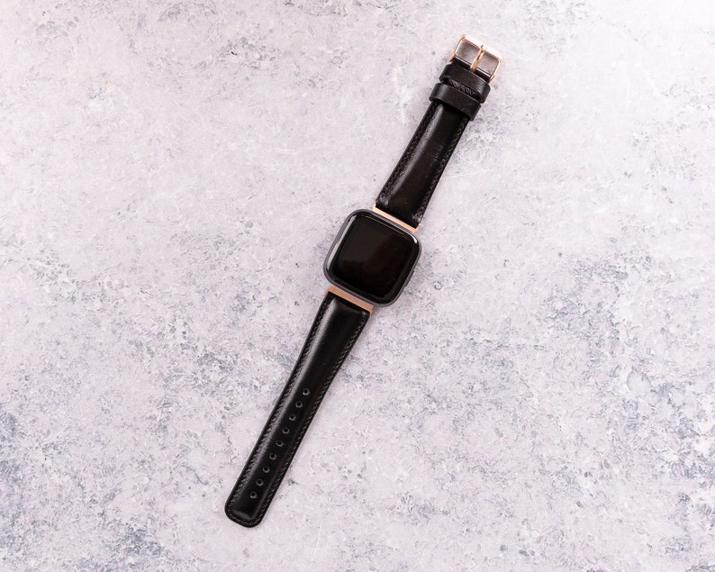 May include: A black leather watch band with a gold buckle and a black square watch face.