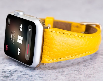 May include: A yellow leather watch band with a silver Apple Watch with the song "Yellow" by Cold Play playing on the screen.